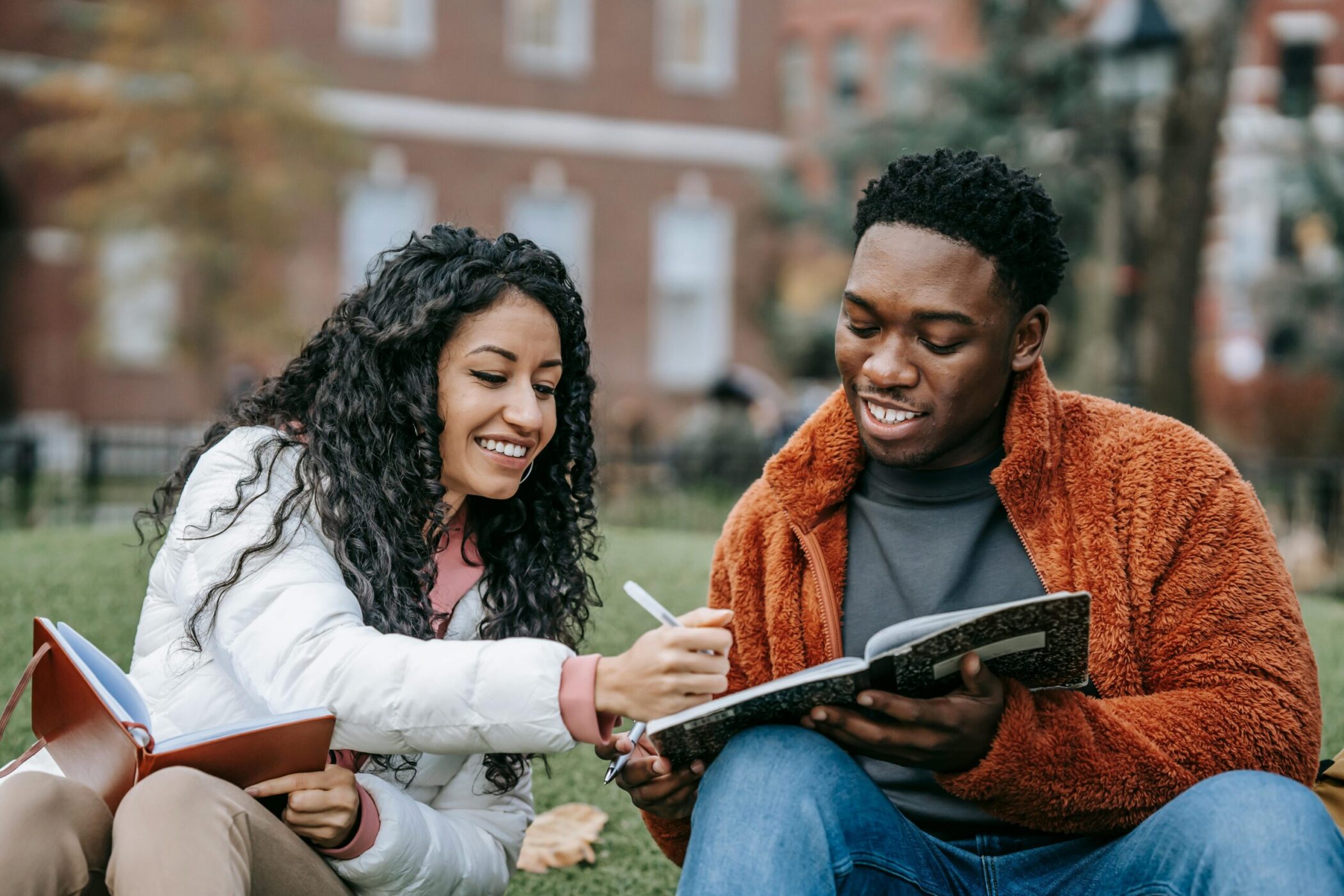 Two young college students sitting on the grass sharing notes