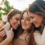 Three adult women smiling and embracing outdoors, representing adult friendships and connection, illustrating how to make friends as an adult and the importance of mental health and relationships, therapy for loneliness, and navigating ADHD and friendships.