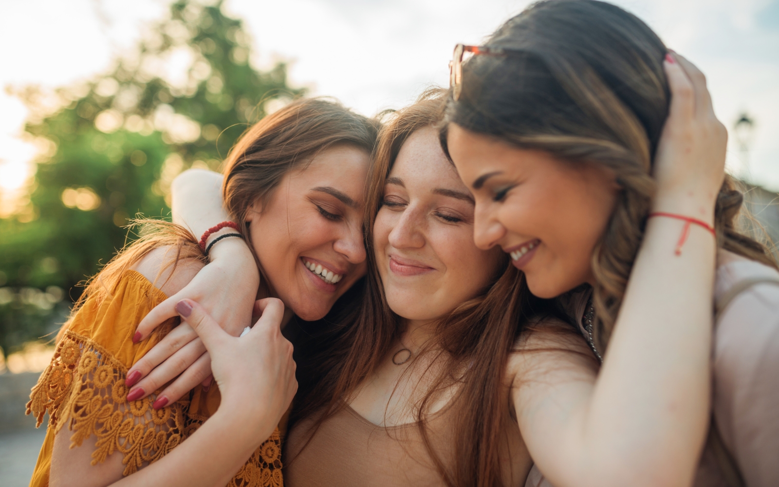 Three adult women smiling and embracing outdoors, representing adult friendships and connection, illustrating how to make friends as an adult and the importance of mental health and relationships, therapy for loneliness, and navigating ADHD and friendships.